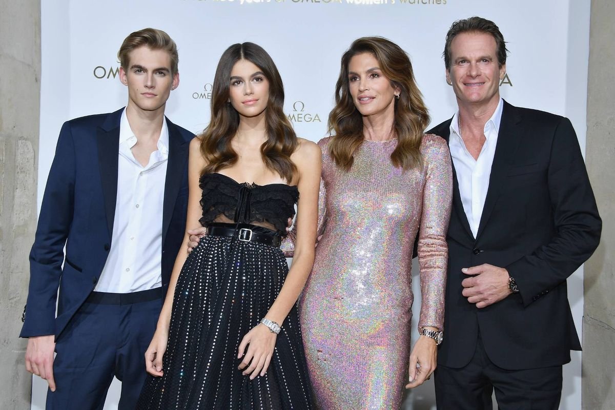 A group of formally dressed individuals, comprising two men and two women, are standing closely together, possibly posing for a photograph at a formal event.